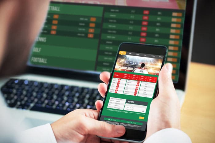 Mann nutzt die Dienste von Sportwetten-Anbietern auf dem Laptop und dem Smartphone